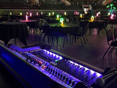 Mixing console lit with purple LEDs overlooking a banquet hall with green uplighting