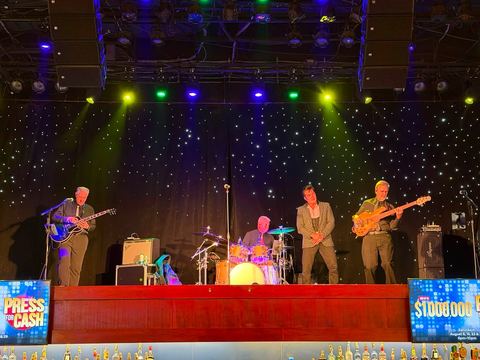 Live band performing on a stage with colored wash lighting and an LED backdrop