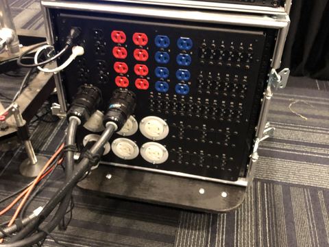 Rolling power distribution rack in a road case with red and blue outlets, rows of breakers, twist-lock outlets and two feeder cables plugged in